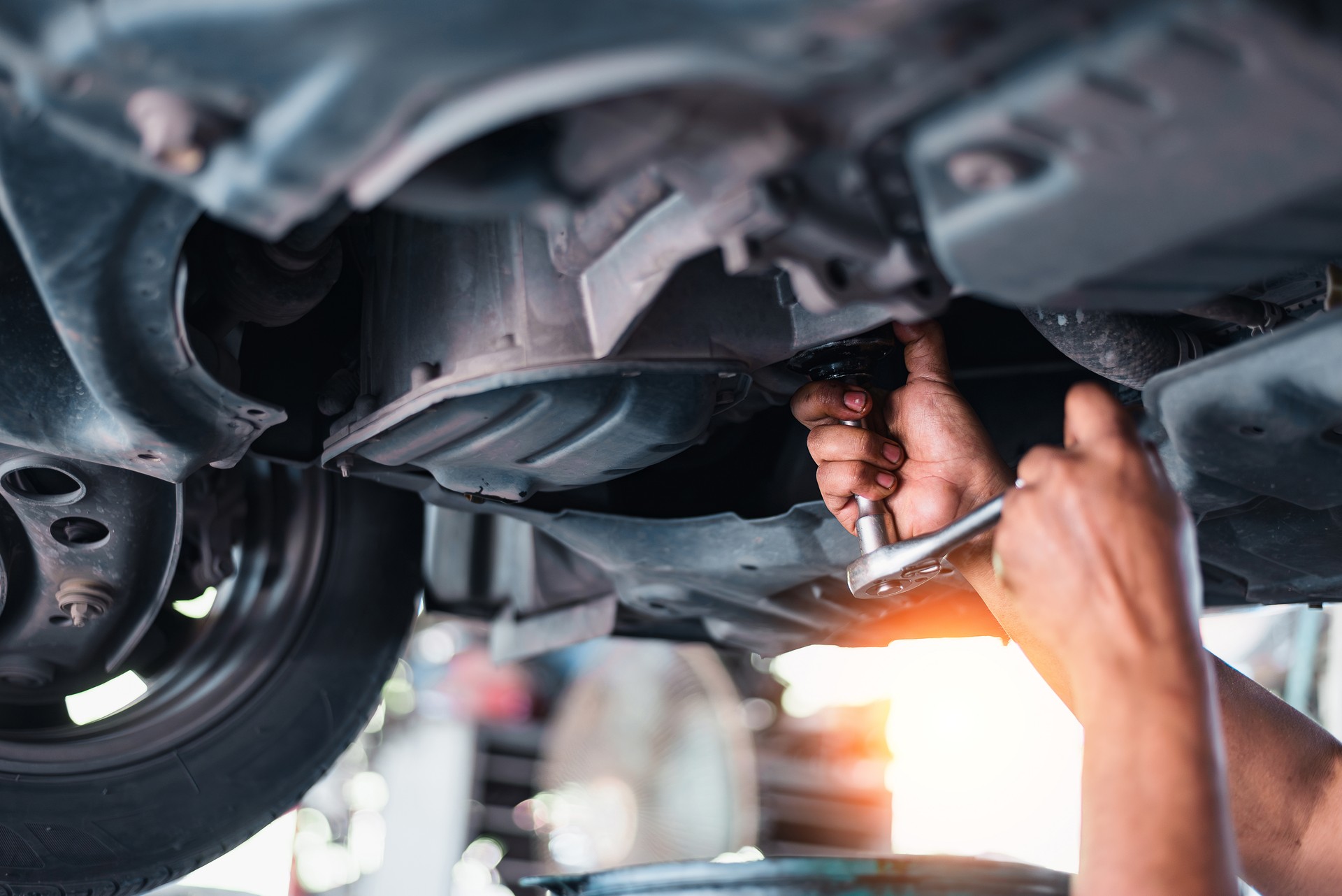 A mechanic in a garage repairs a car engine, oil-stained hands working with tools