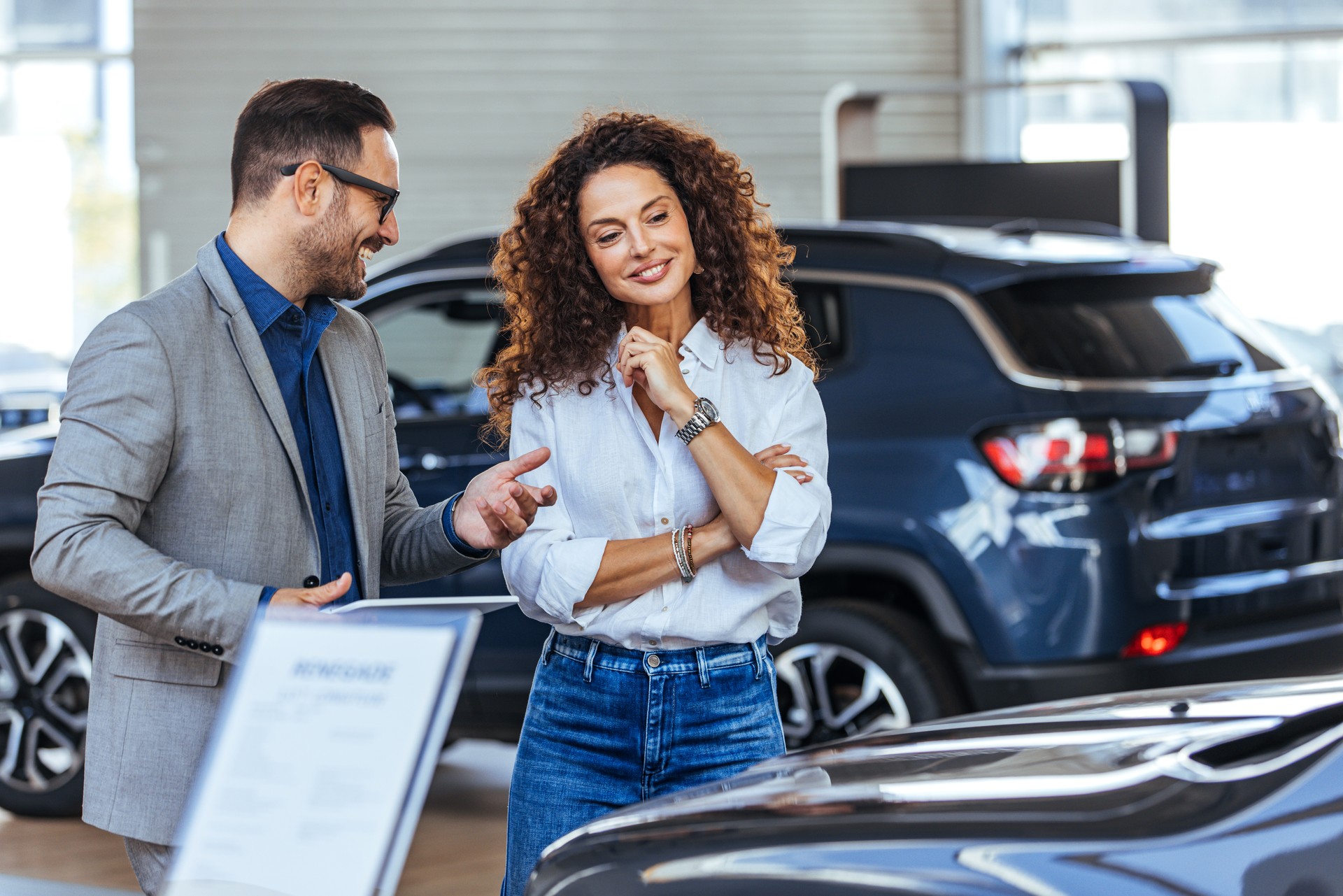 Happy salesman selling the car to his female customer in a showroom.